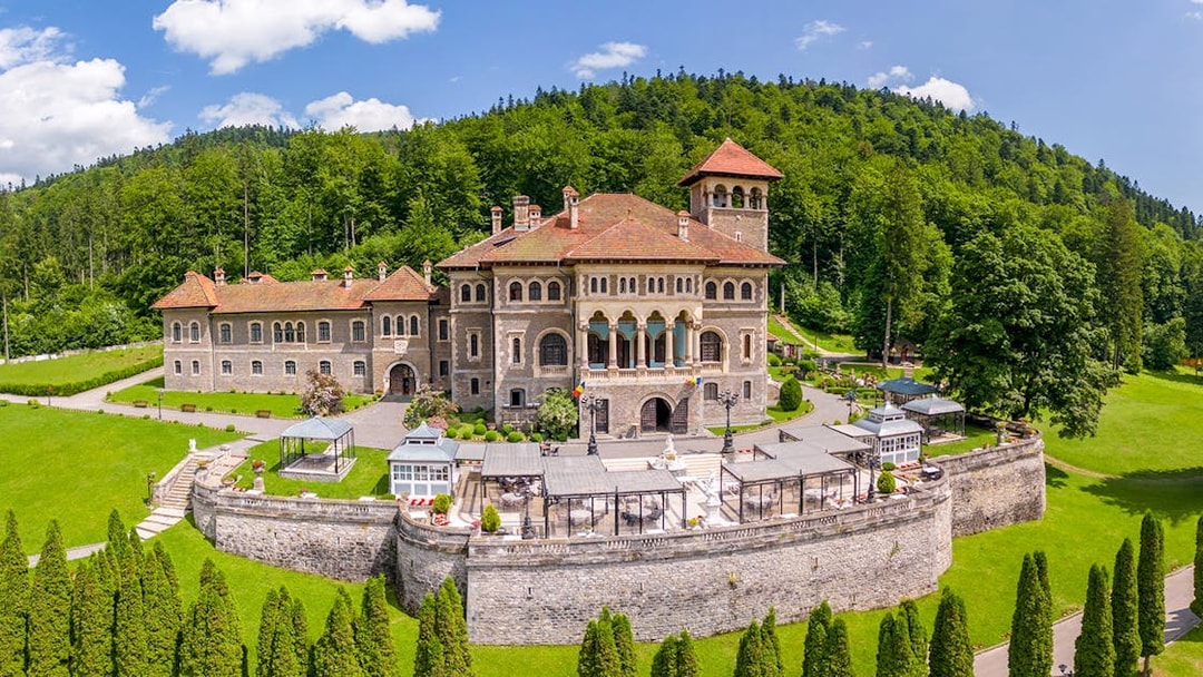 Cantacuzino Castle exterior with lush gardens and forest backdrop in Romania.