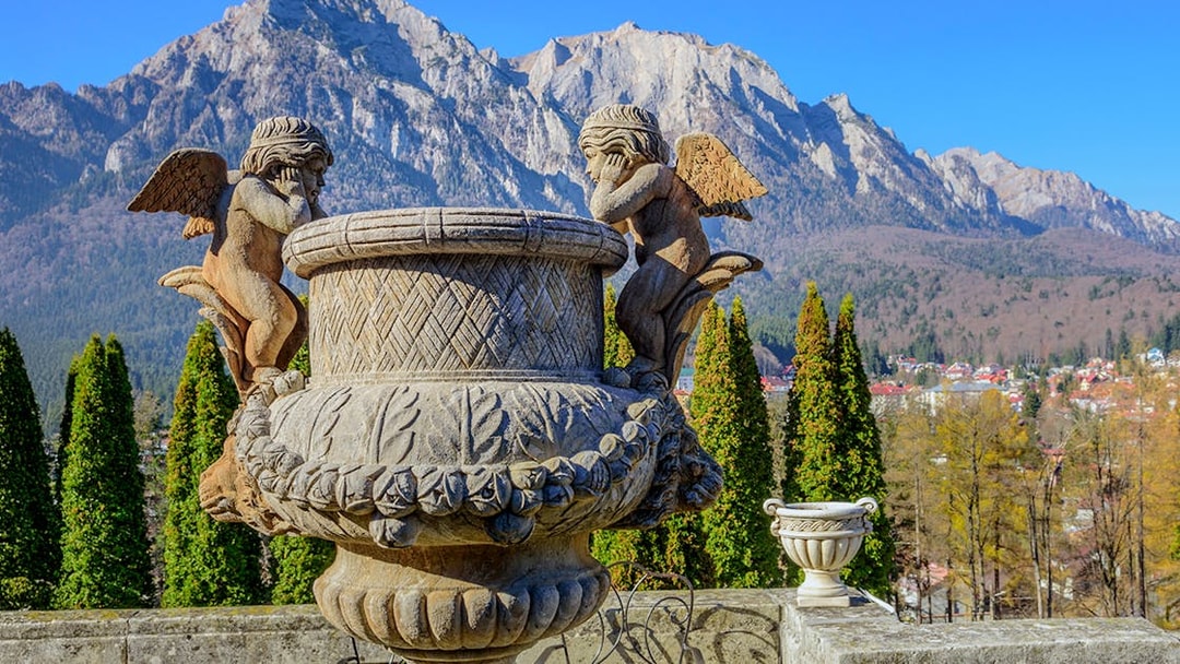 Sculpture of cherubs inside Cantacuzino Palace with mountain backdrop.