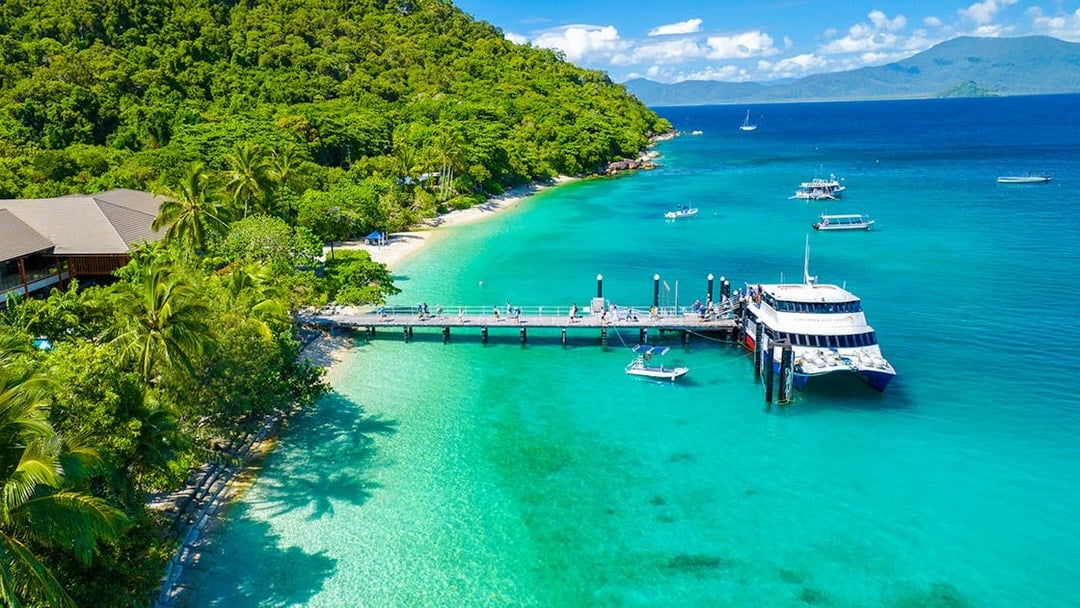 Fitzroy Island pier with tour boat, clear waters, and lush greenery, Cairns day trip.