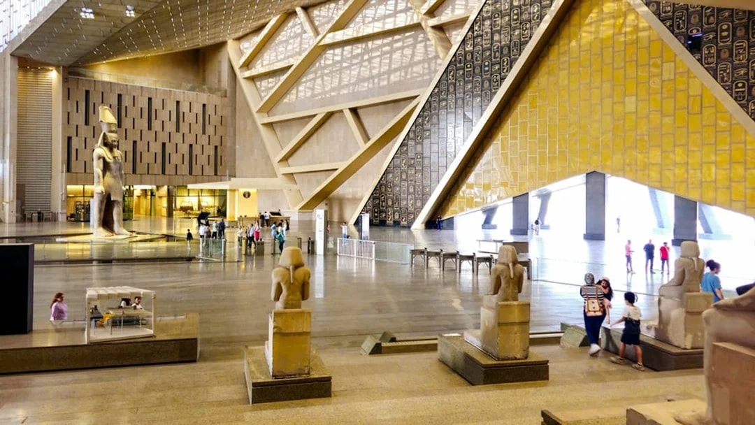 Grand Egyptian Museum interior with ancient statues and visitors in Cairo.