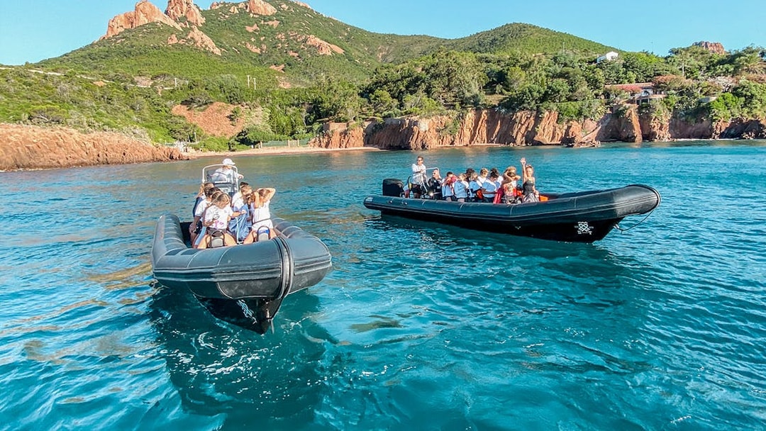 Two boats with tourists exploring Estérel natural park's coastline near Cannes.