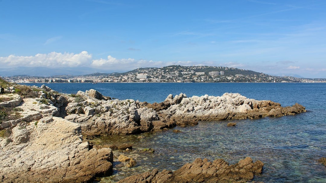 Rocky coastline of Ste. Marguerite Island with Cannes in the background across the sea.
