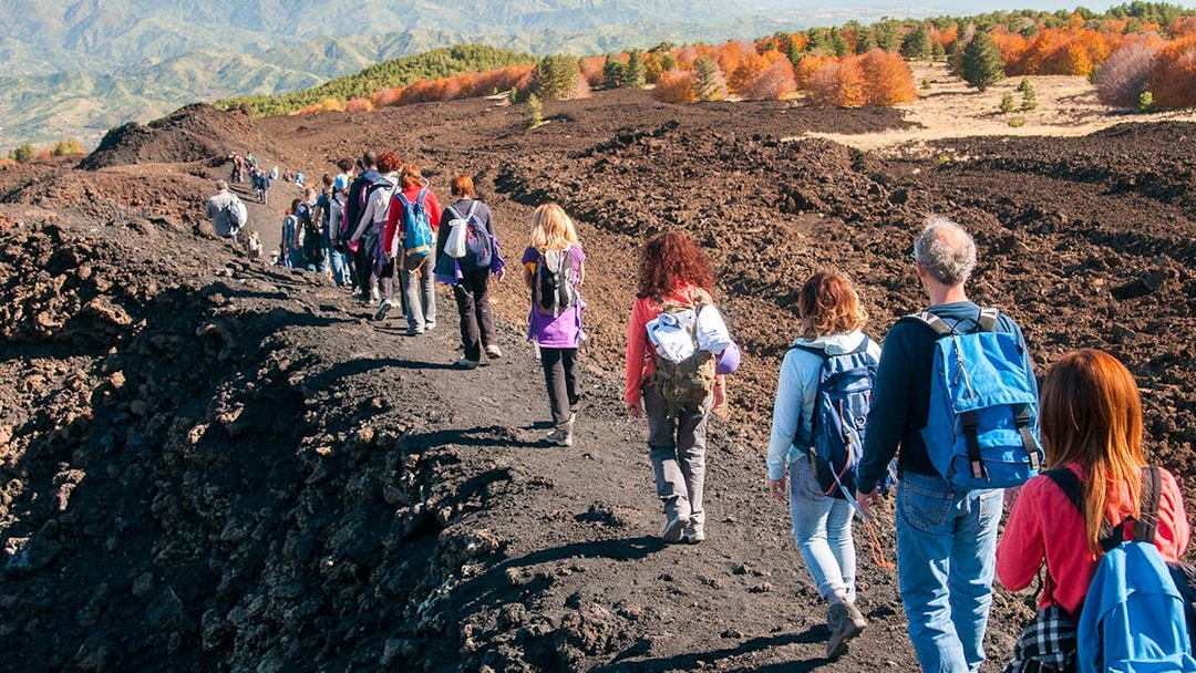 Group hiking on Mount Etna's volcanic terrain during afternoon guided tour.