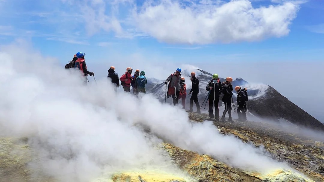 Group hiking on Mount Etna summit with volcanic steam vents.