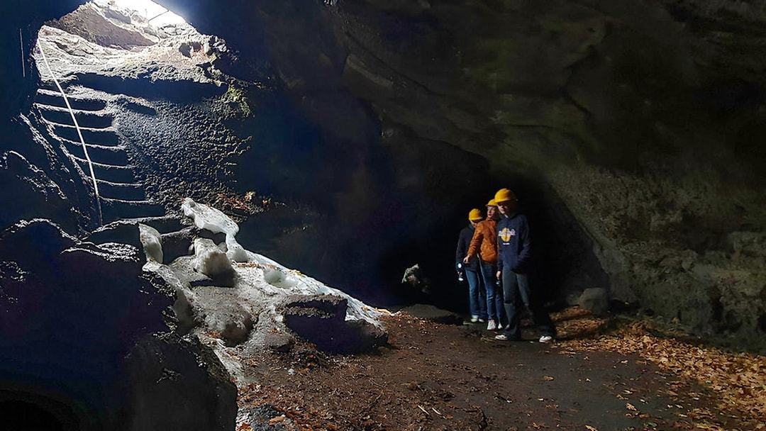 Tourists with a guide exploring a lava cave with icy formations and a stone staircase.