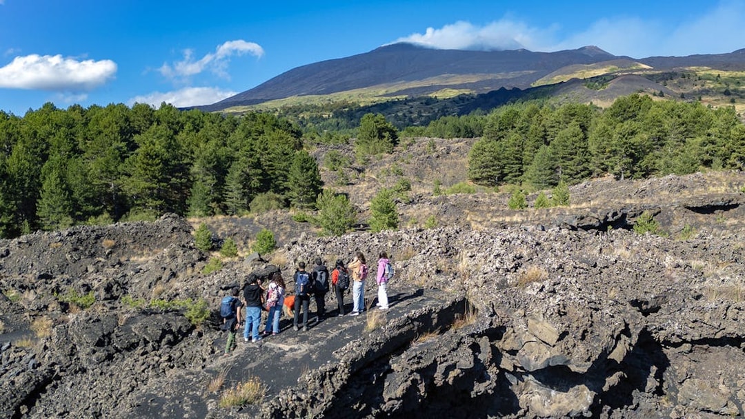 Tourists exploring lava caves near Mount Etna with forested landscape.