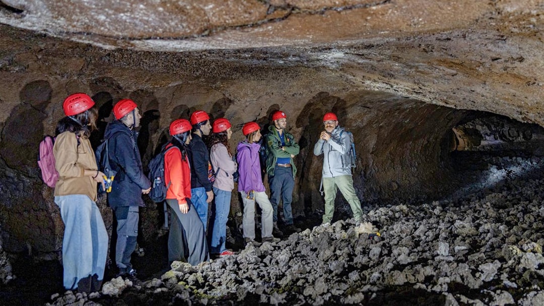 Tour group exploring lava caves near Mount Etna with a guide.