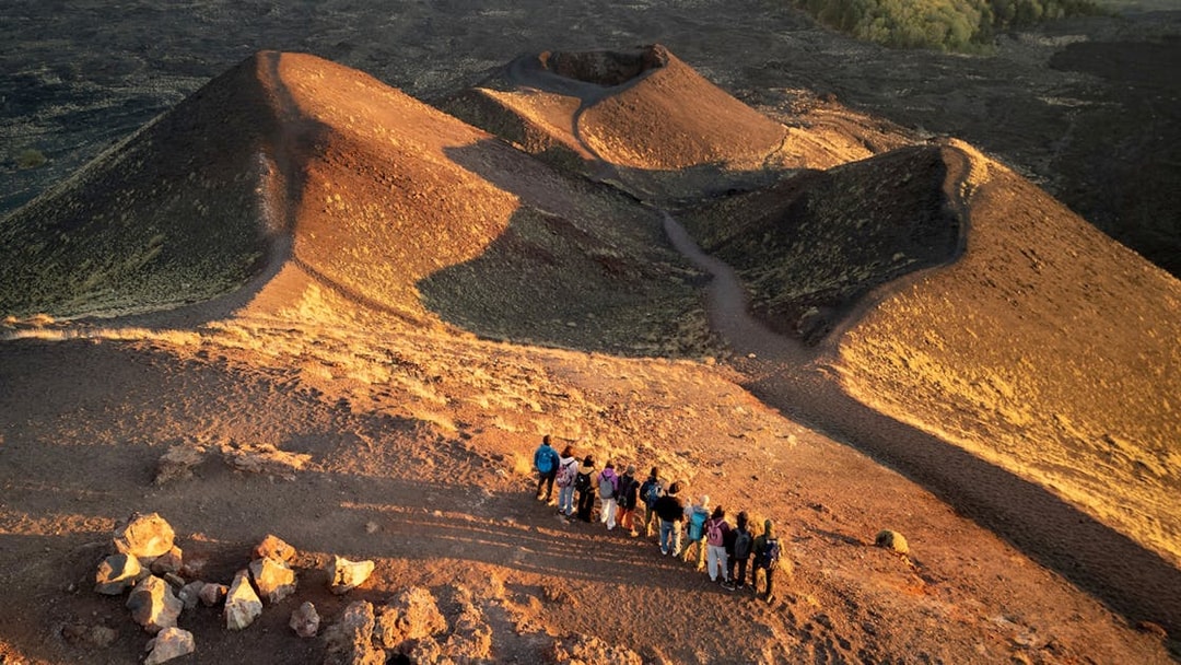 Tourists on Mount Etna at sunset, viewing volcanic craters and landscape.