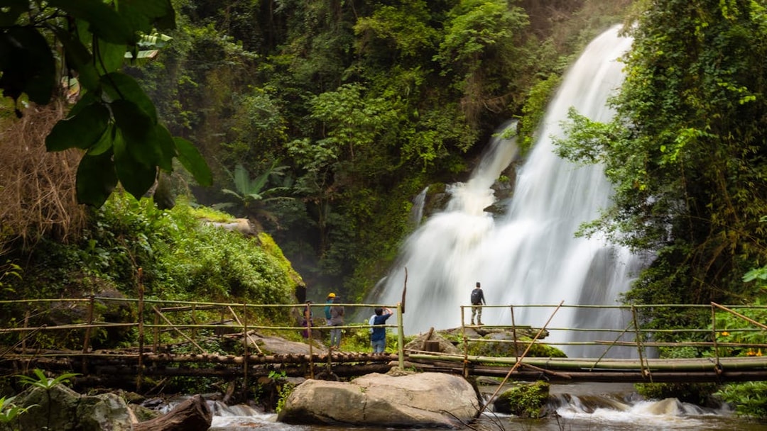 Visitors on a bamboo bridge near Pha Dok Siew waterfall in lush forest.