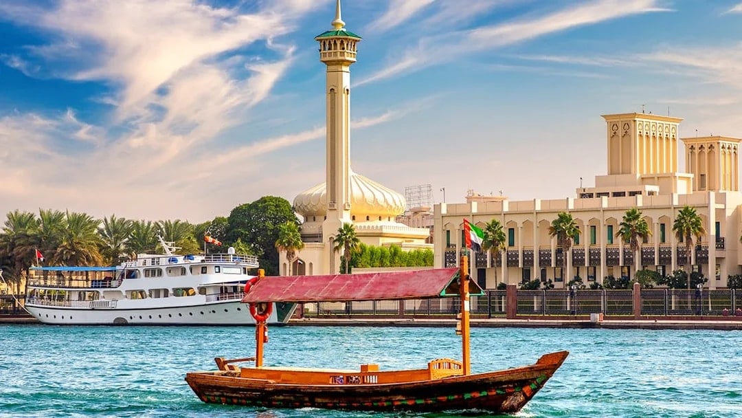 Wooden Abra boat on Dubai Canal with mosque and buildings in the background.