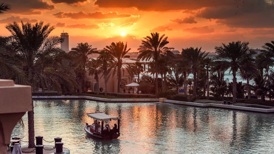 Abra boat on Dubai Water Canal at sunset with palm trees and skyline.