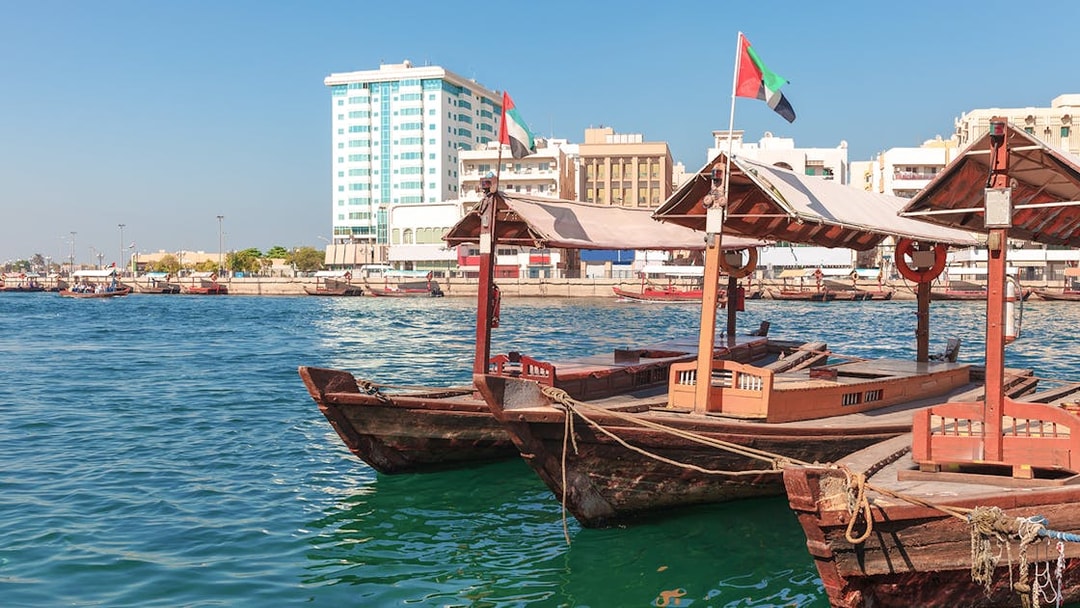 Traditional Abra boat docked at Dubai Creek pier with cityscape in the background.
