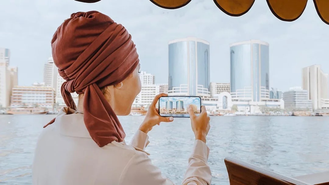 Woman photographing skyline from Abra Dhow boat on Dubai Creek.
