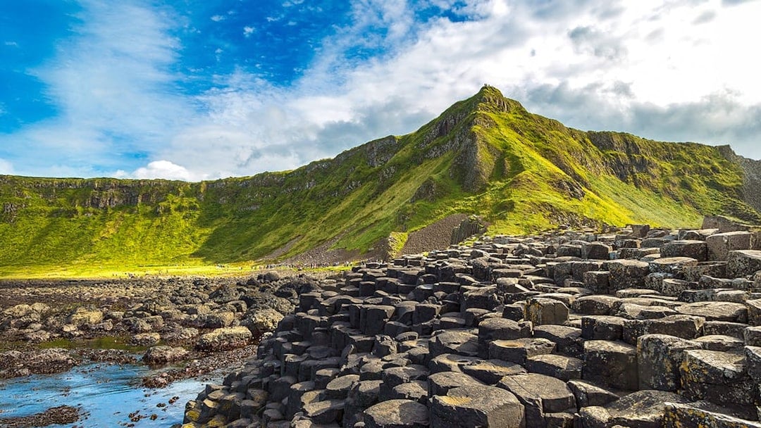 Giant's Causeway basalt columns with green cliffs in Northern Ireland.