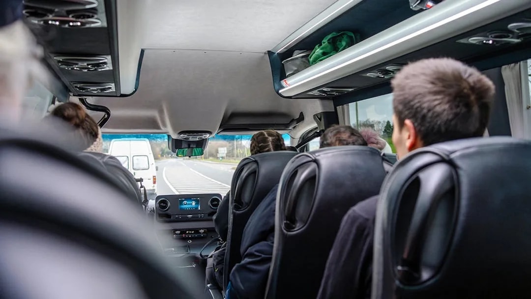 Inside view of a guided bus tour with passengers seated, traveling on a highway.