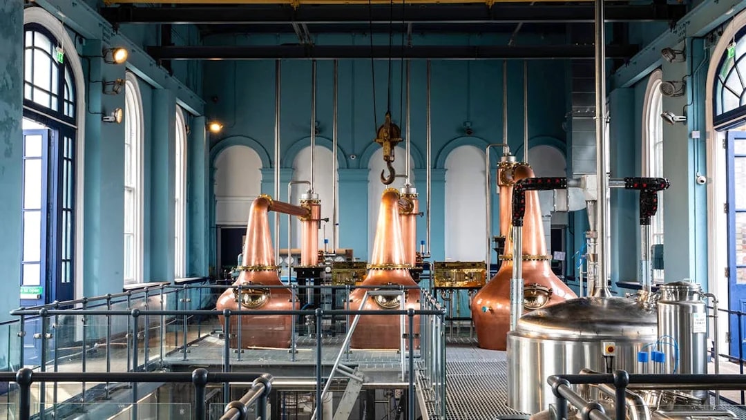 Copper stills inside Titanic Whiskey Distillery with arched windows and industrial equipment.