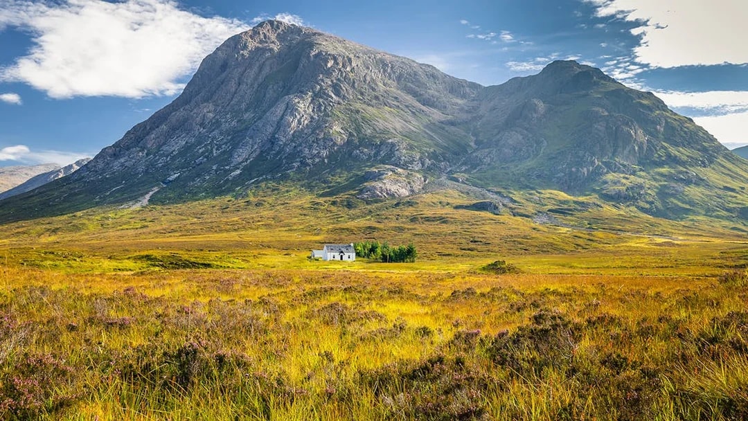 Remote hut amidst lush greenery and mountains in Glencoe, Scotland.