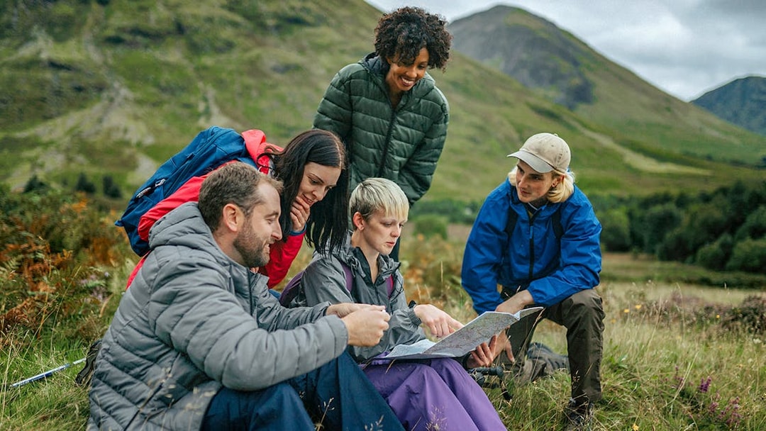 Tour guide explaining map to tourists in a scenic mountain landscape.