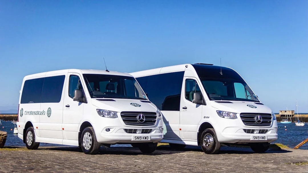 Private air-conditioned transfer vans parked by a waterfront.