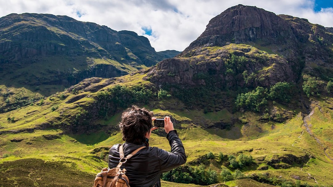 Tourist photographing the Three Sisters of Glencoe, Scotland.