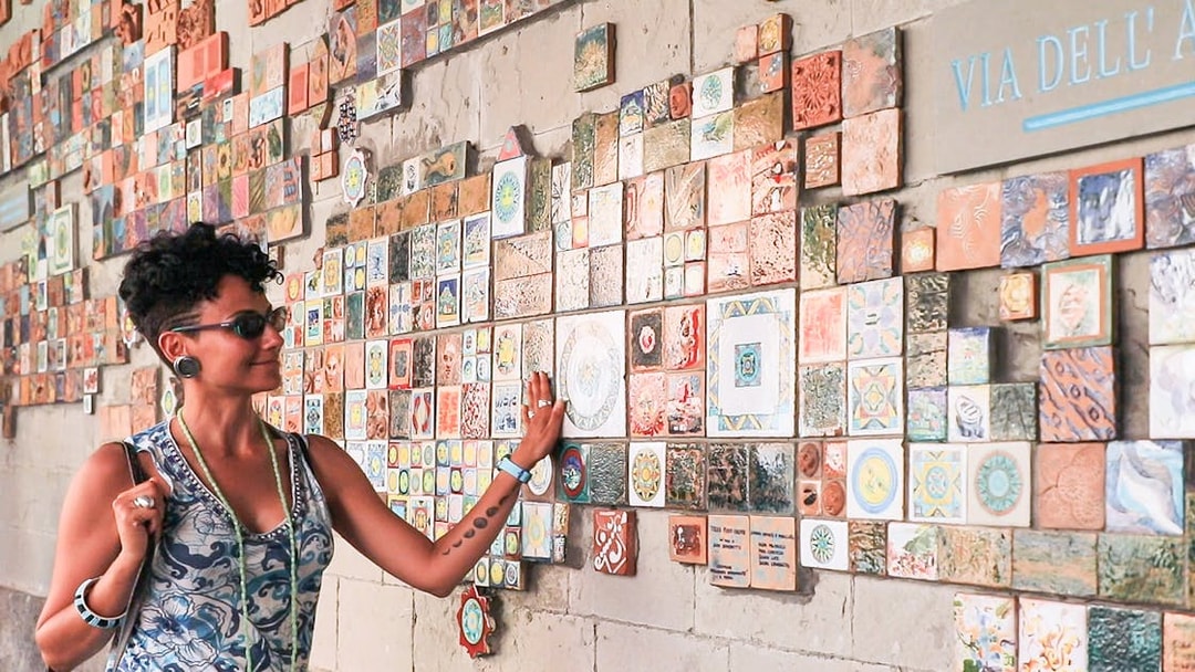 Woman admiring colorful tiles on a wall in Via dell'Arte, Italy.