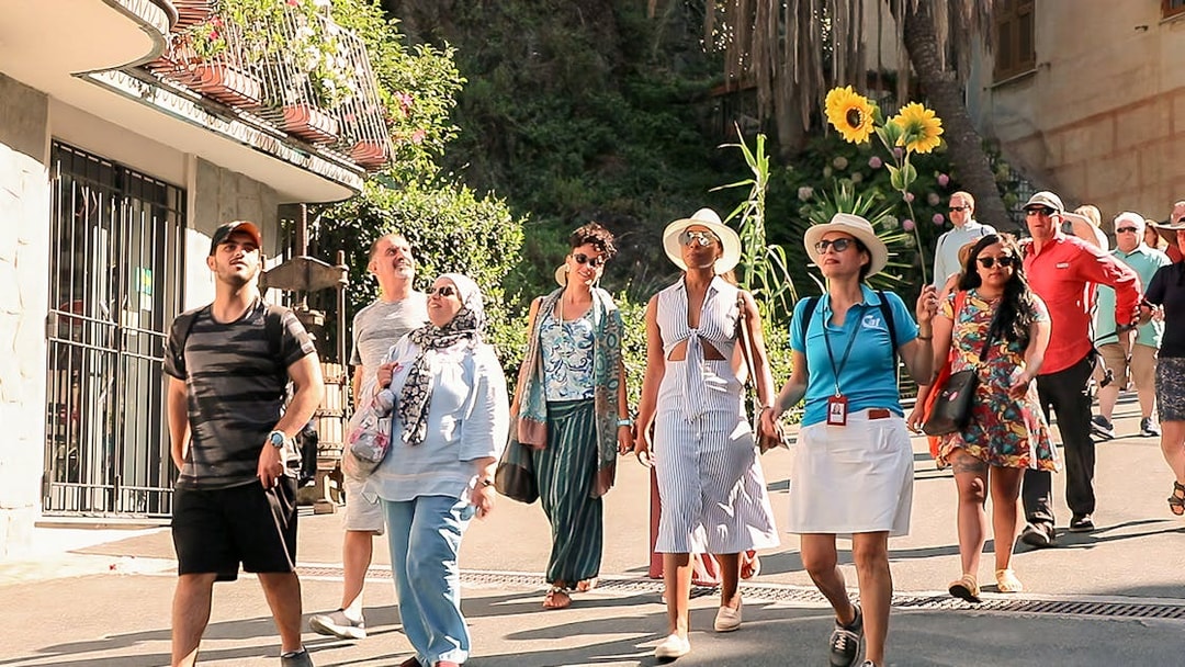 Tour group exploring Cinque Terre village street on a sunny day.