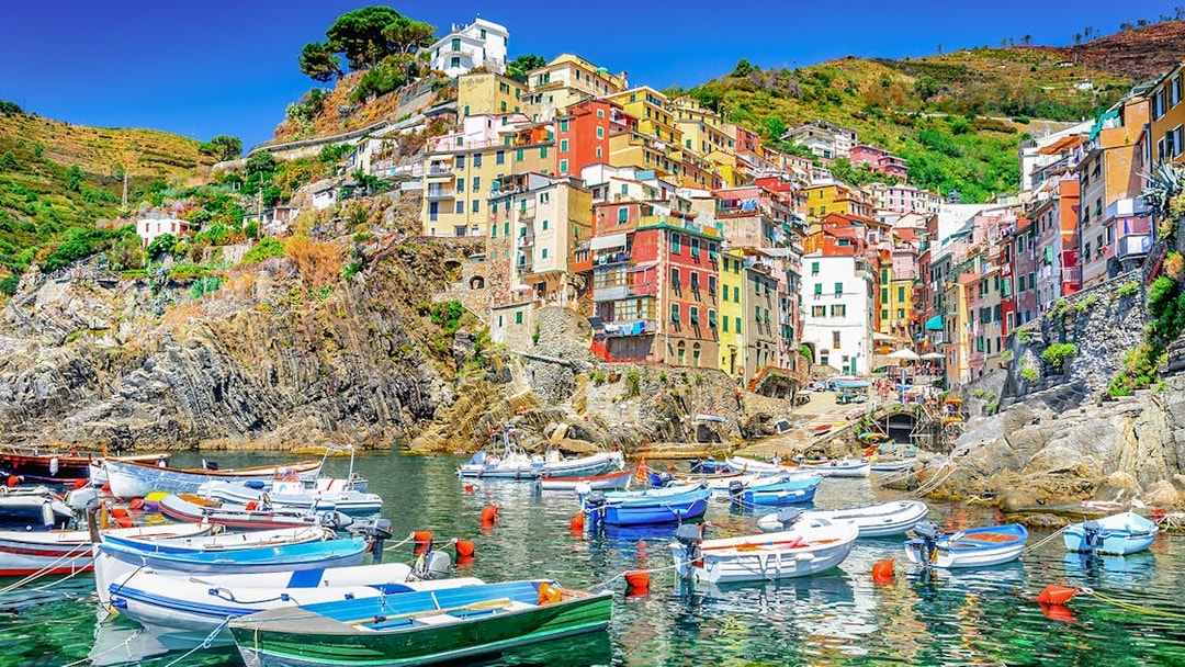 Boats in the harbor of Riomaggiore, Cinque Terre, with colorful hillside buildings.
