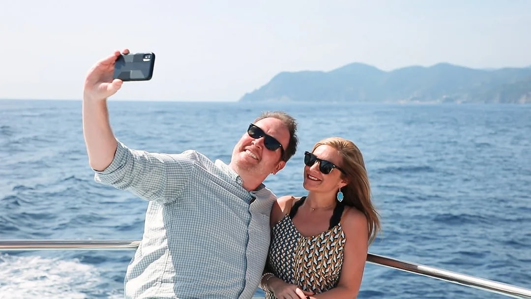 Couple taking a selfie on a boat with ocean and mountains in the background.