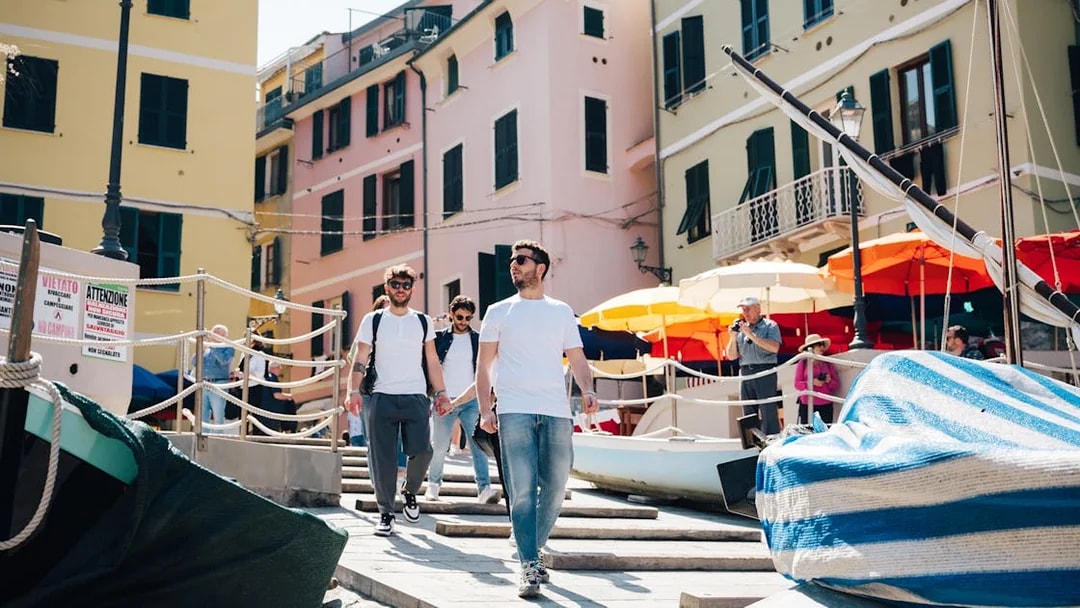 Tourists walking through colorful streets of Cinque Terre, Italy, with boats and umbrellas nearby.
