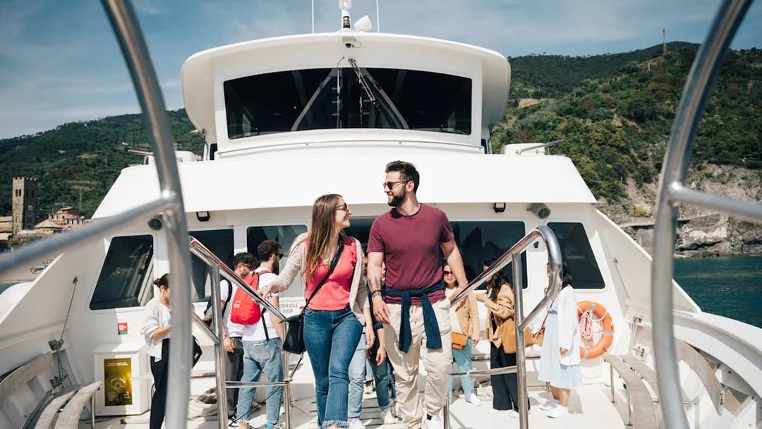 Couple walking on a boat deck with Cinque Terre coastline in the background.