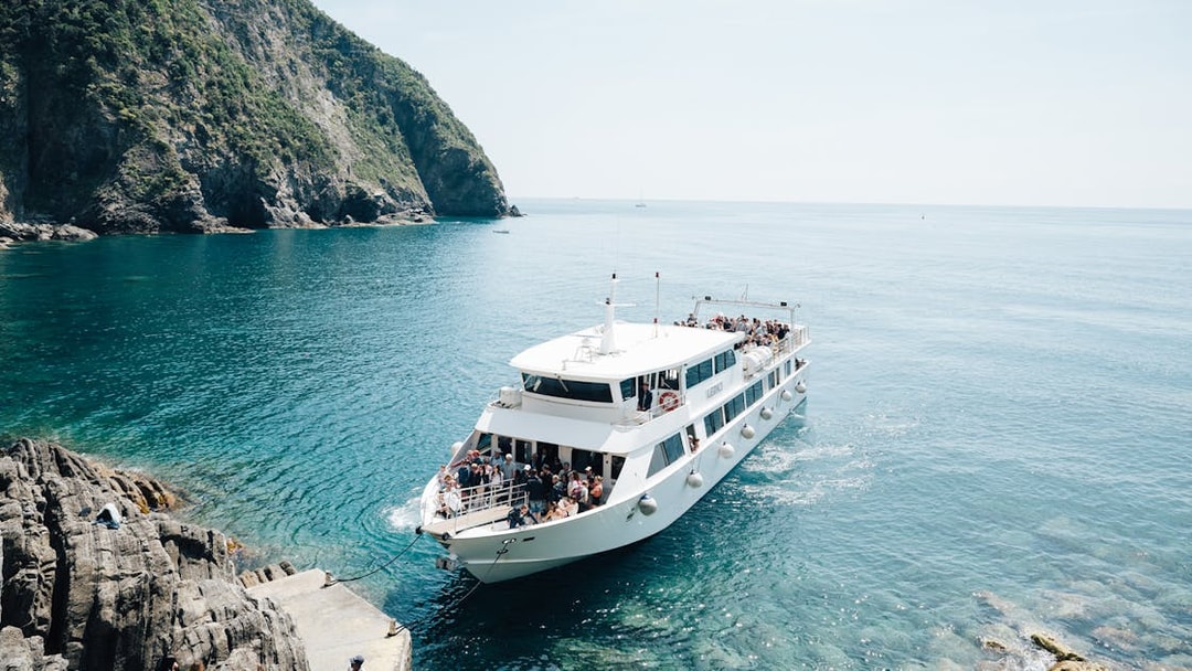 Boat arriving at rocky shore in Cinque Terre, Italy, with passengers on deck.