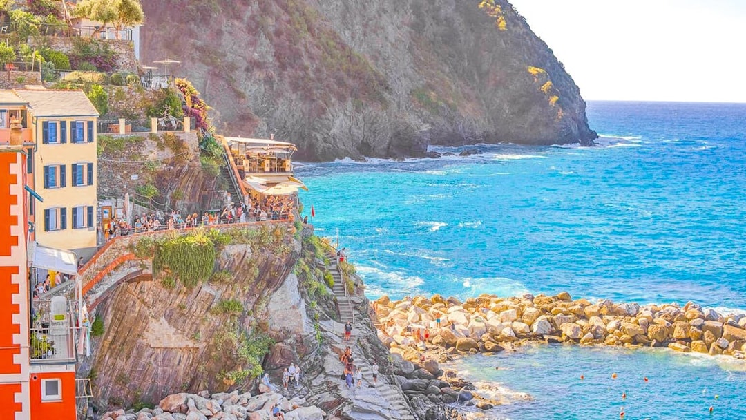 Cliffside view of colorful buildings and tourists in Cinque Terre, Italy, overlooking the sea.