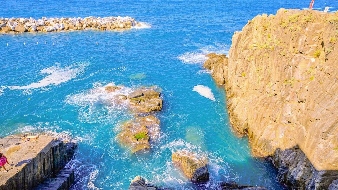 Rocky coastline and clear blue sea in Cinque Terre, Italy, viewed from a cliff.