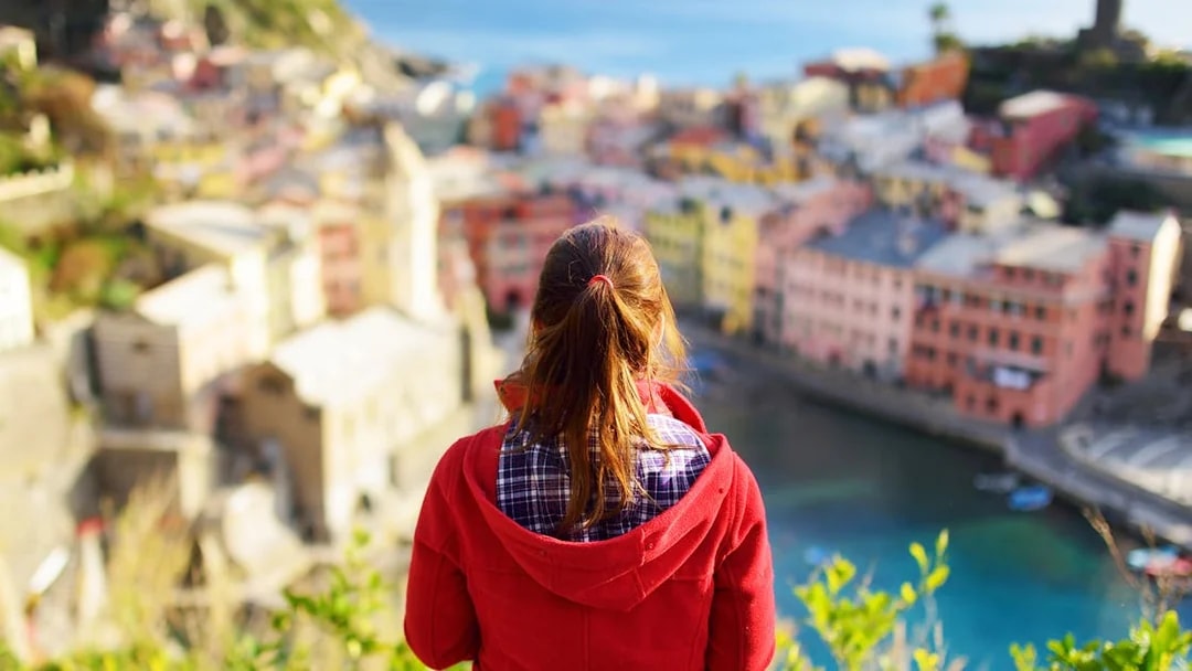 Person overlooking colorful buildings and coastline in Cinque Terre, Italy.