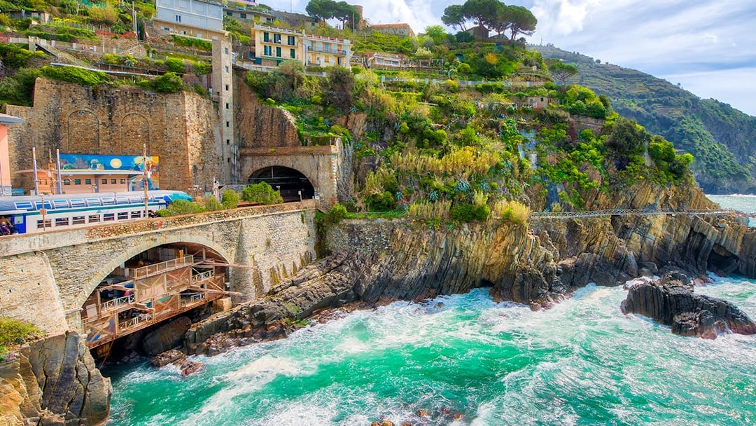 Train passing through coastal cliffs in Cinque Terre, Italy, with colorful hillside houses.