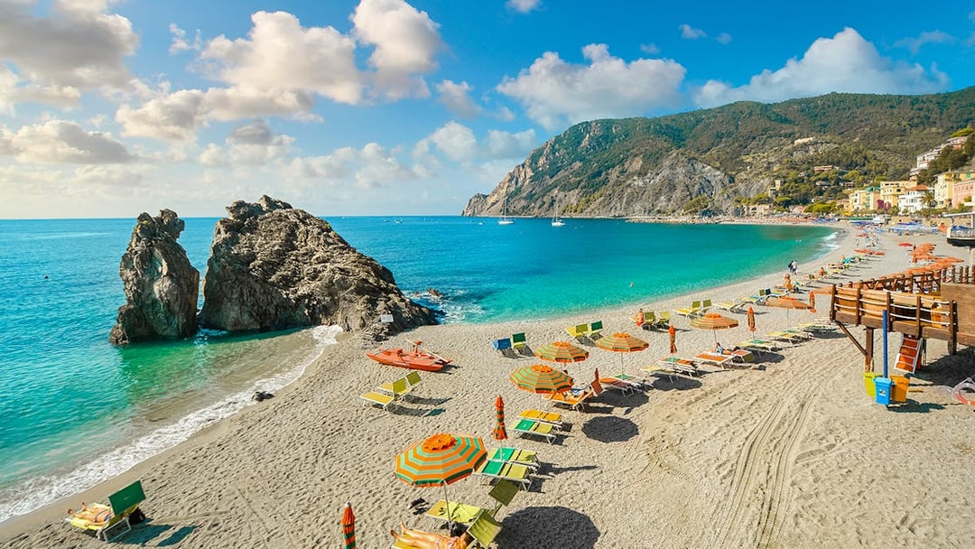 Beach with colorful umbrellas and sunbathers in Cinque Terre, Italy, part of a guided tour from Florence.