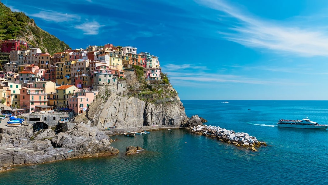 Colorful houses on a cliff in Cinque Terre with a boat in the sea, part of Florence to Cinque Terre tour.