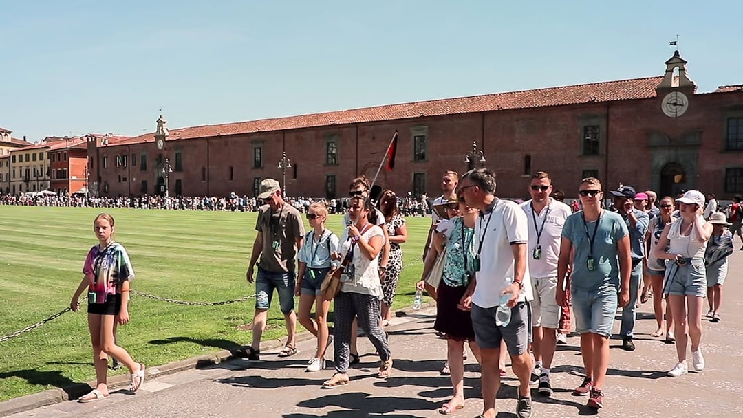 Tour group walking in Pisa with a guide holding a flag, part of a guided tour from Florence.