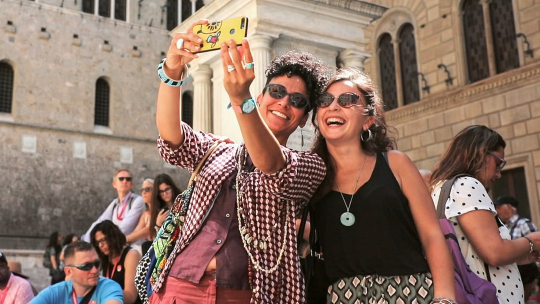 Tourists taking a selfie in front of a historic building in Siena, Italy.