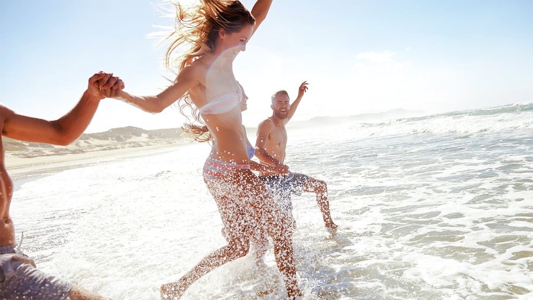 Guests enjoying a beach day, splashing in the ocean waves.