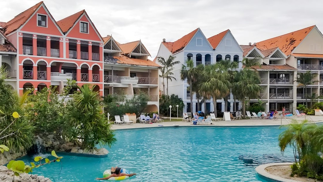 Taino Beach Resort pool area with colorful buildings and palm trees in the background.