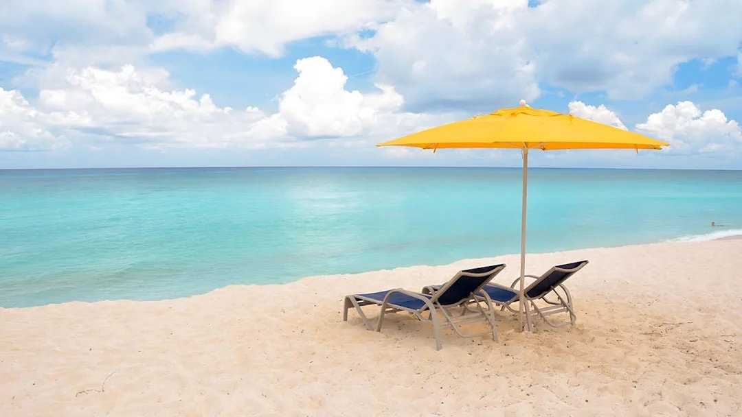 Two lounge chairs under a yellow umbrella on a sandy beach in Bimini, Bahamas.