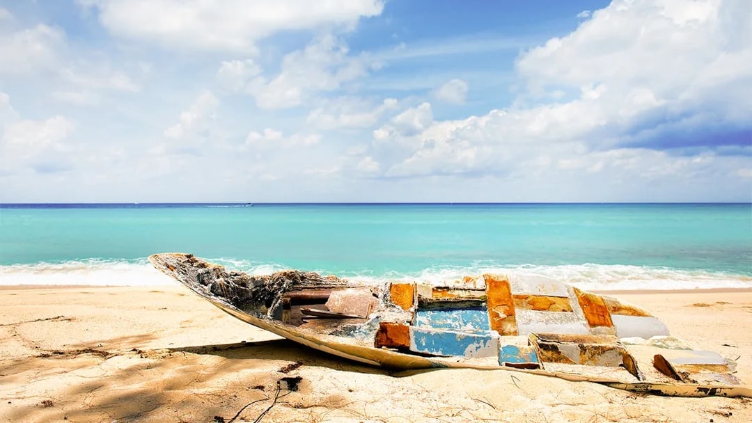Abandoned boat on a sandy beach with turquoise water in Bimini, Bahamas.