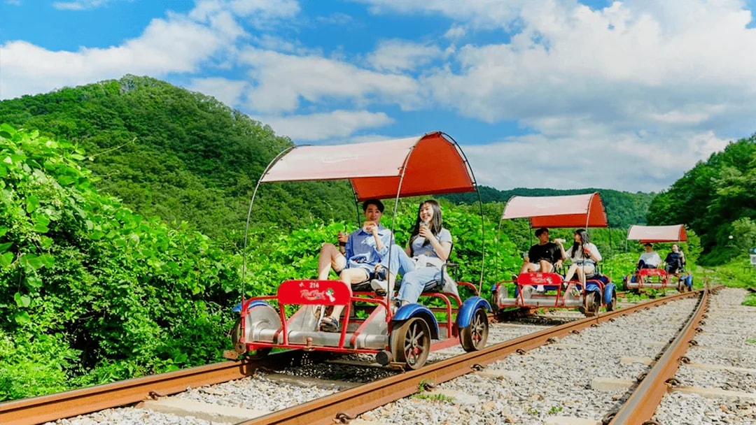 Couple enjoying Gangchon Gimnyujeong Rail Bike ride through lush greenery.