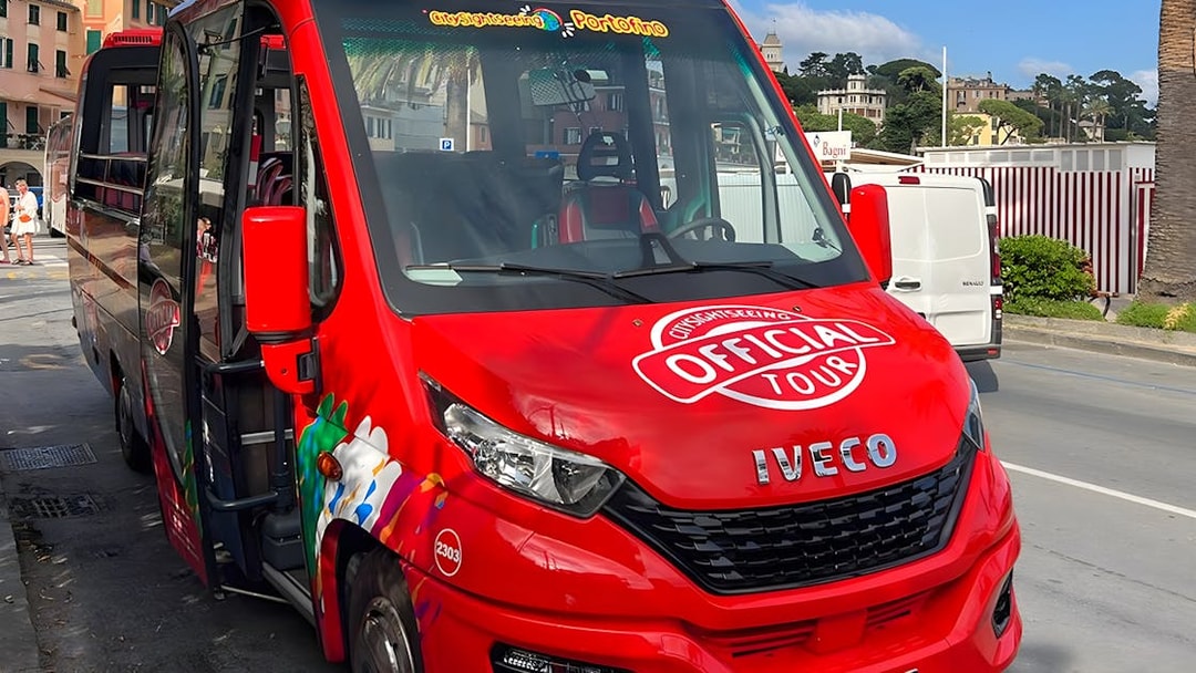 Red tour bus for day trip from Genova to Portofino parked on street.
