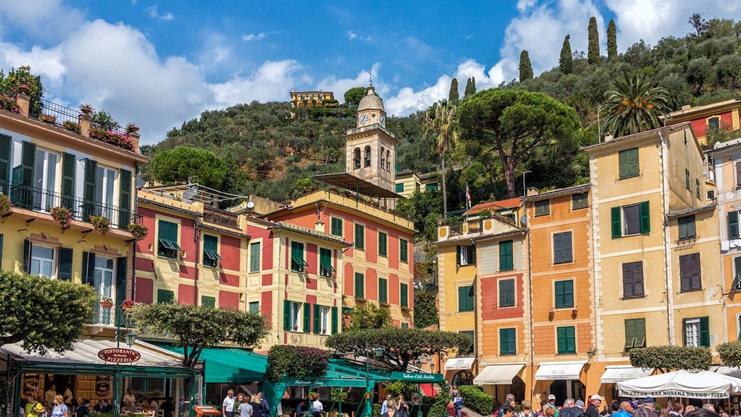 Colorful buildings and a clock tower in Portofino, Italy, with tourists exploring the area.