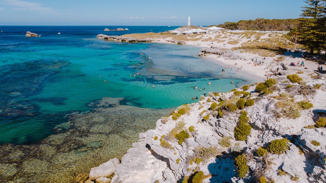 Tourists swimming at a beach on Rottnest Island with a lighthouse in the distance.