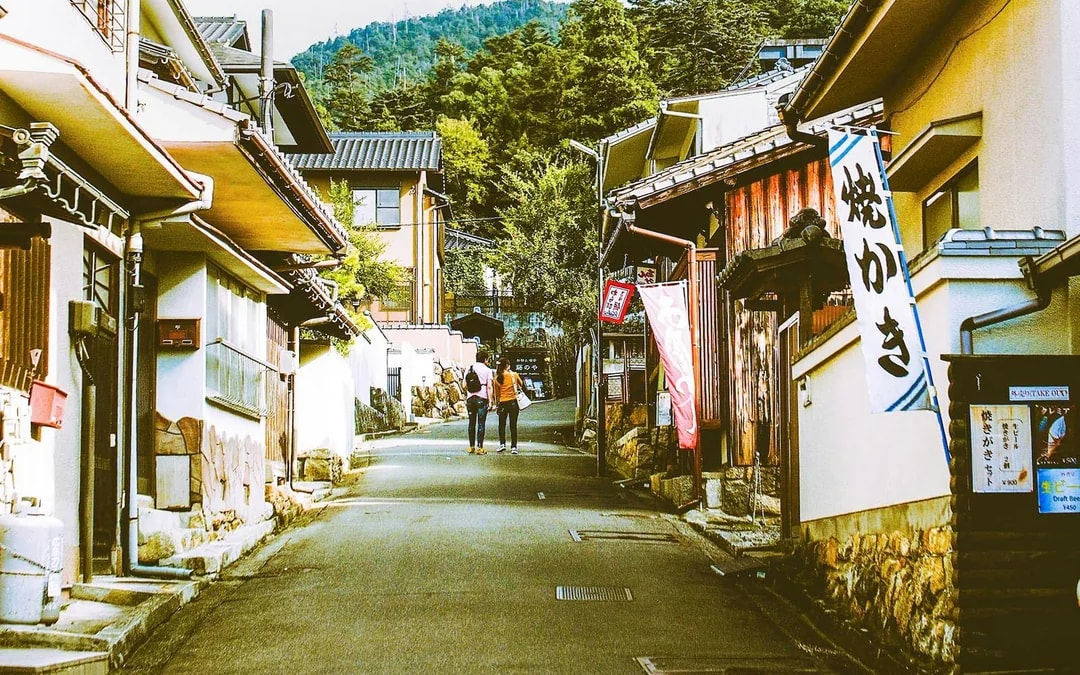 Street view of traditional buildings on Miyajima Island, Japan, with two people walking.