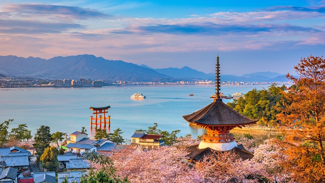 Miyajima Island view with Itsukushima Shrine's torii gate, cherry blossoms, and pagoda, Hiroshima, Japan.