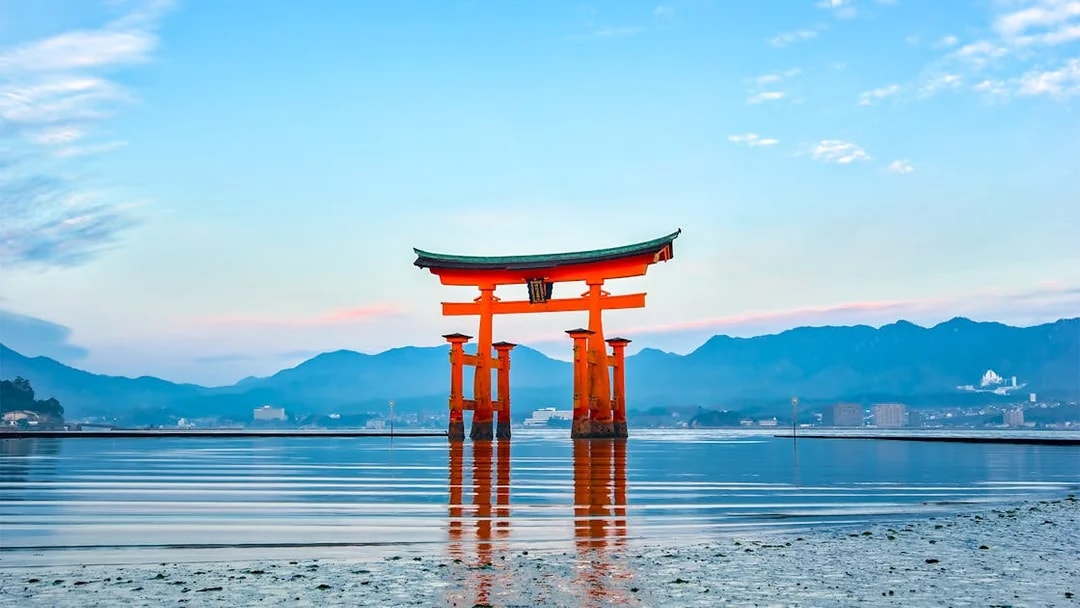 Torii gate at Itsukushima Shrine, Hiroshima, viewed from the water with mountains in the background.